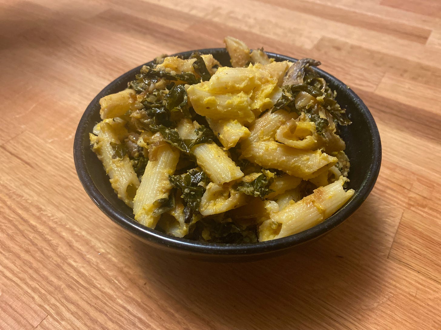 A ceramic bowl of full of penne with thick butternut squash sauce sits on a wooden counter.