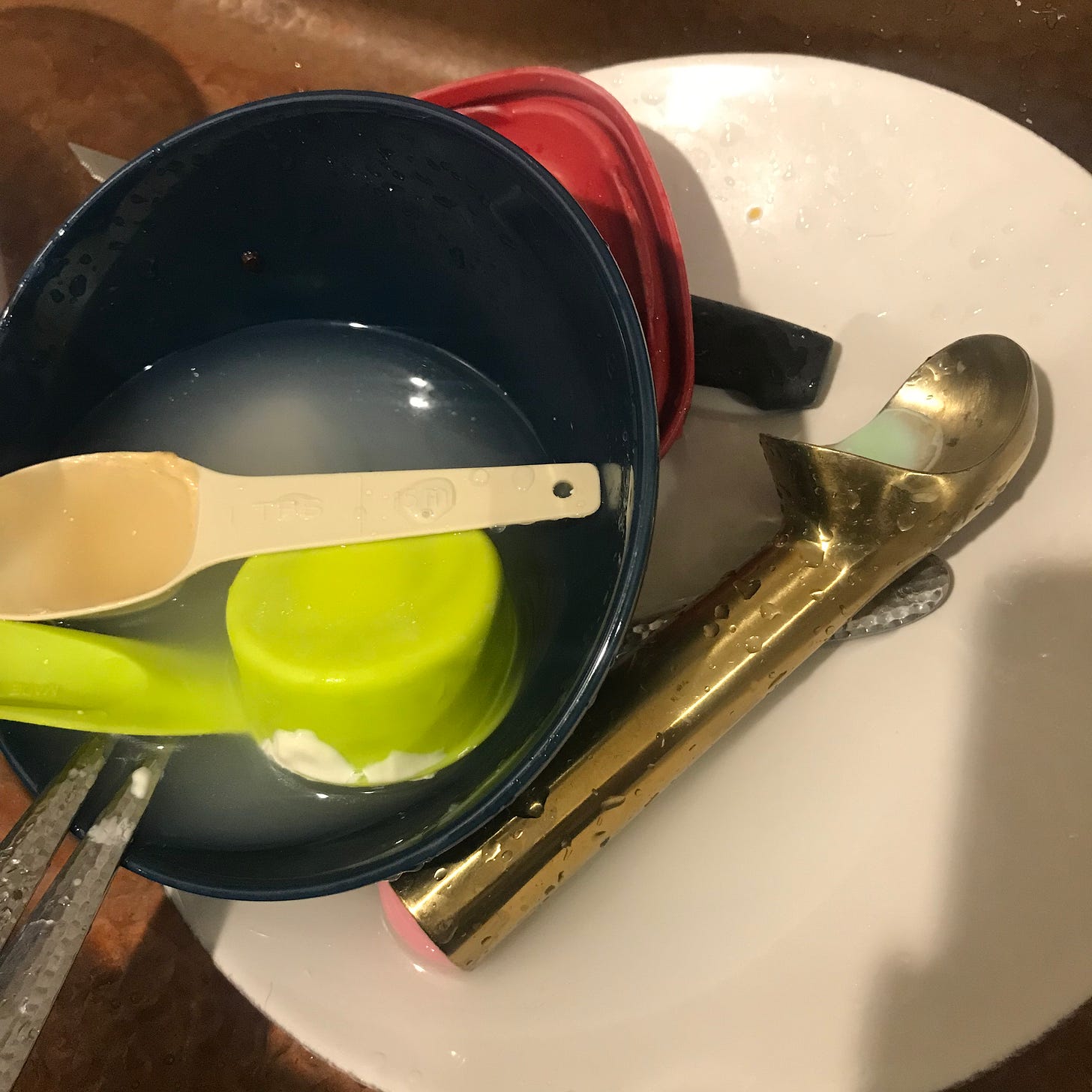 Close up of dirty dishes in a sink with a focus on a gold and pink ice cream scoop.