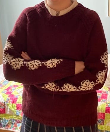 a burgundy knit sweater with white snowflakes on the arms