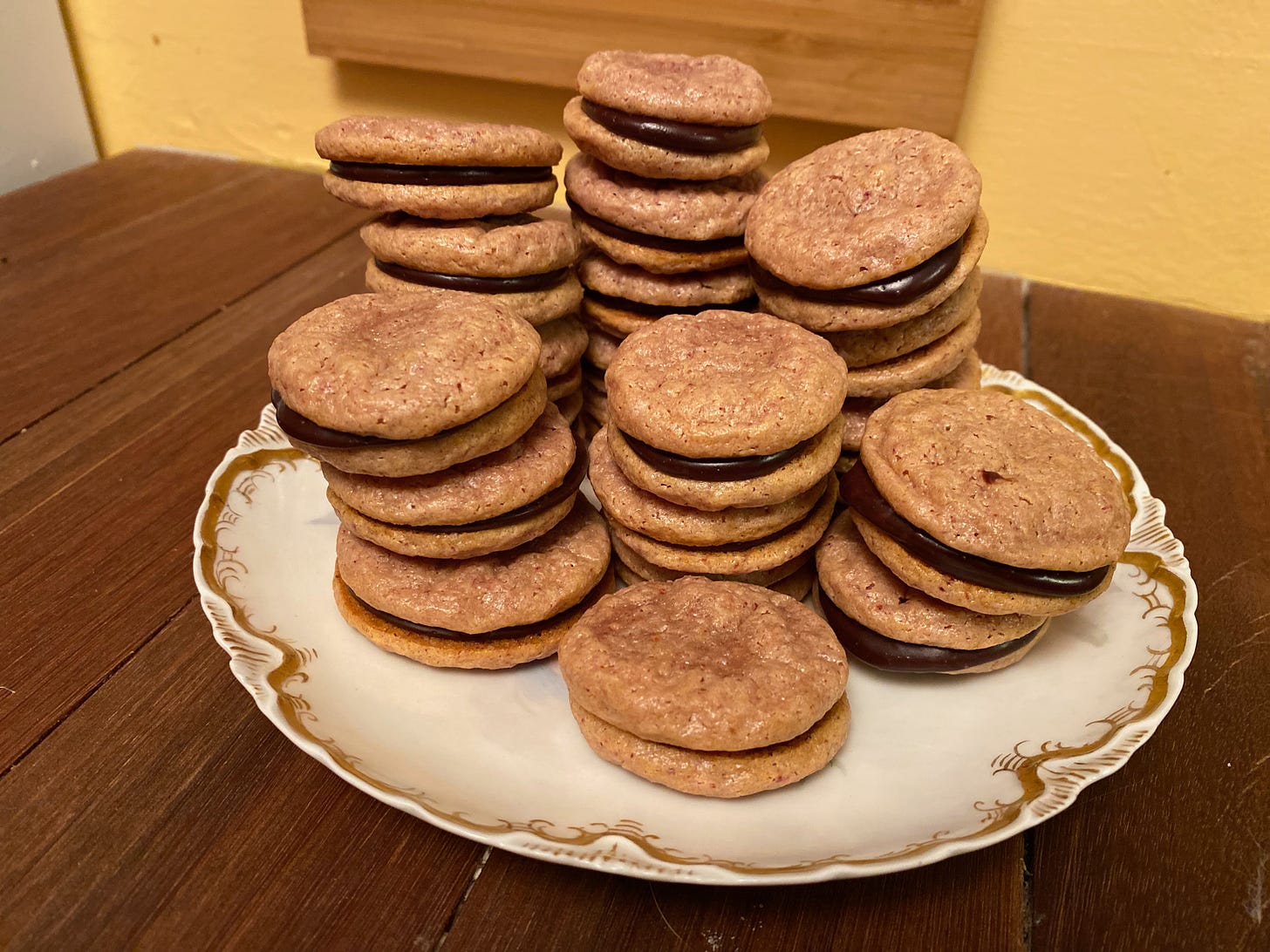 Several stacks of small round sandwich cookies sit on a ceramic plate on a wooden counter.
