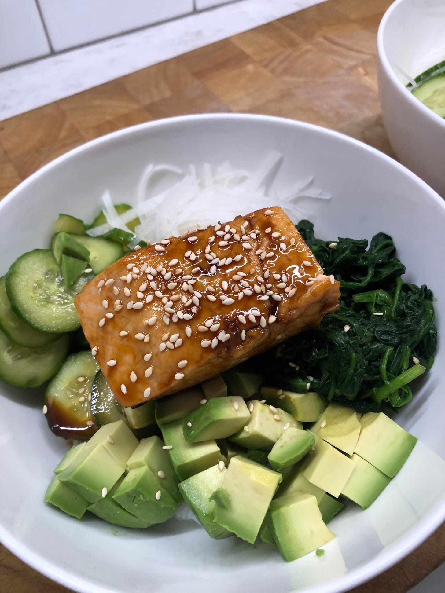A bowl of rice topped with salmon teriyaki, cucumbers, avocado, spinach, and daikon