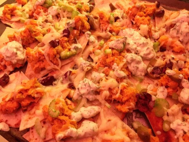 A pan of nachos with melted cheese, olives, celery, and dots of white ranch dressing.