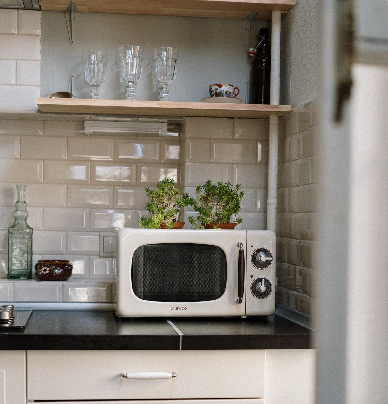 Image of a white Daewoo brand microwave on a black kitchen countertop with a white tile backsplash.