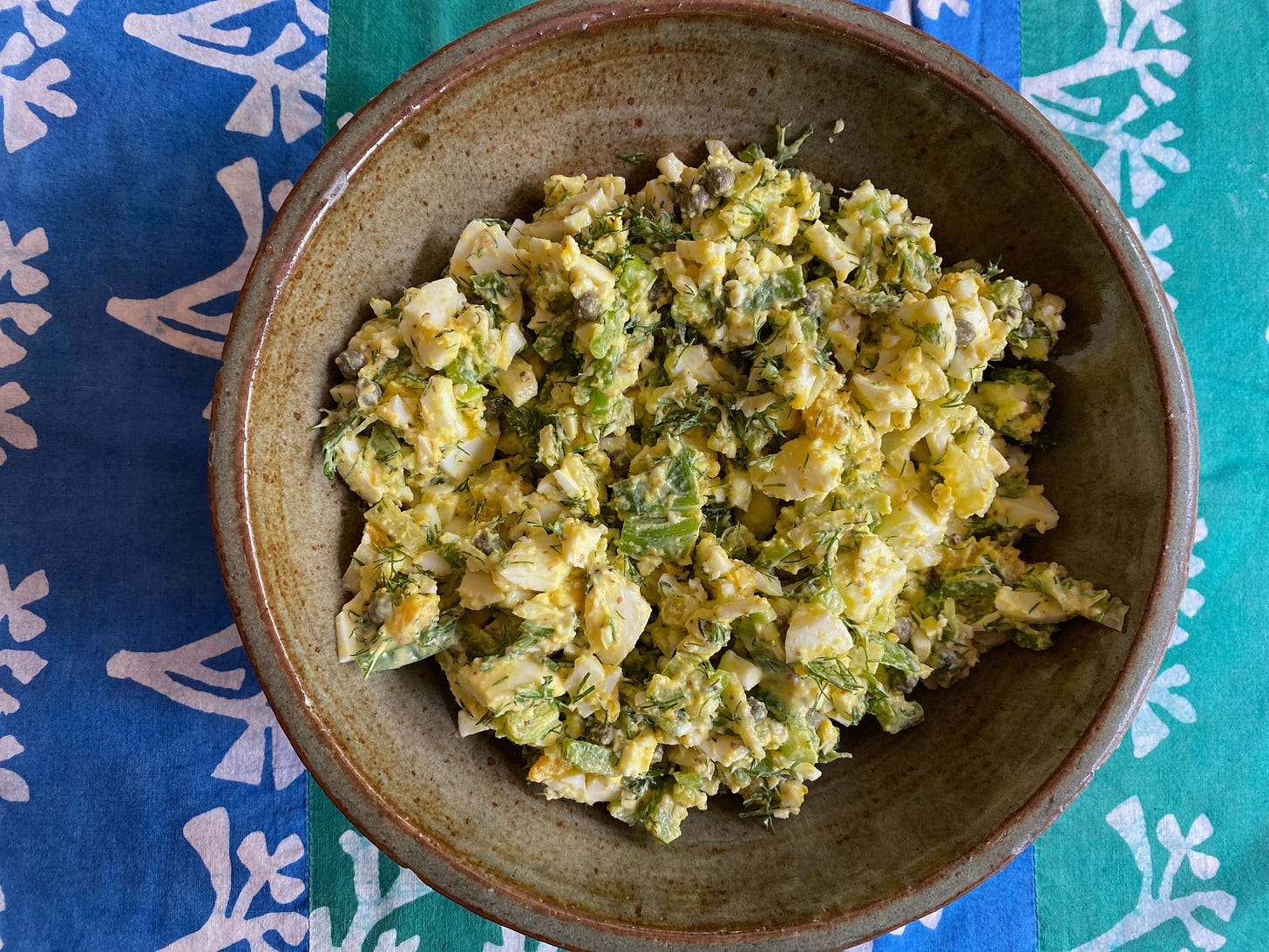 A ceramic bowl of egg salad on a blue and green striped placemat.