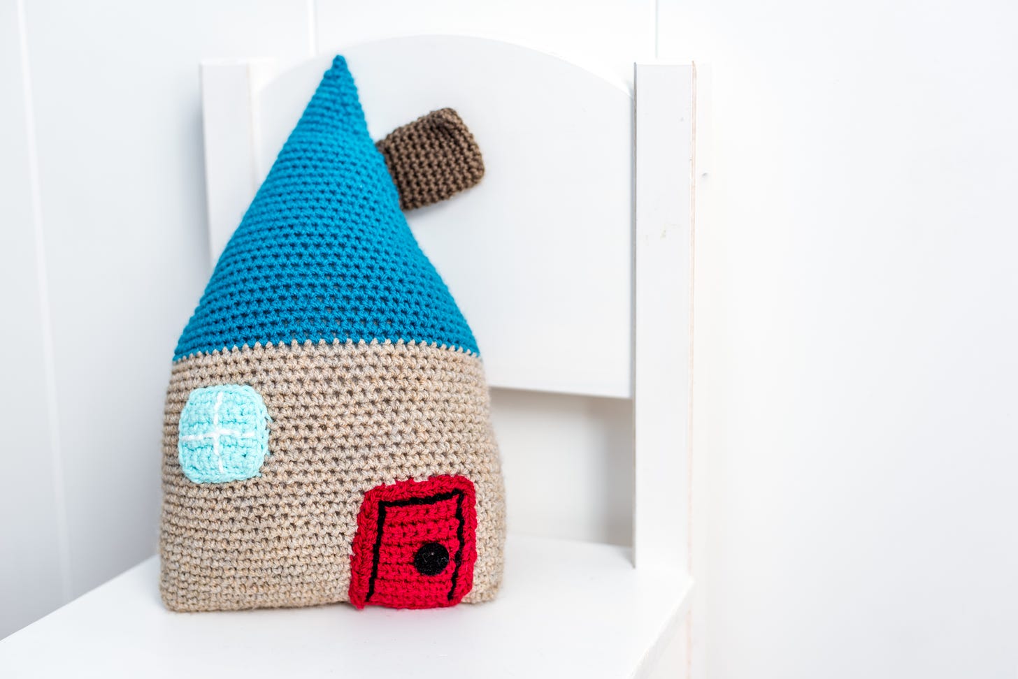A small knit fairy house with a red door, blue roof and brown chimney. It looks dumb but I want it.