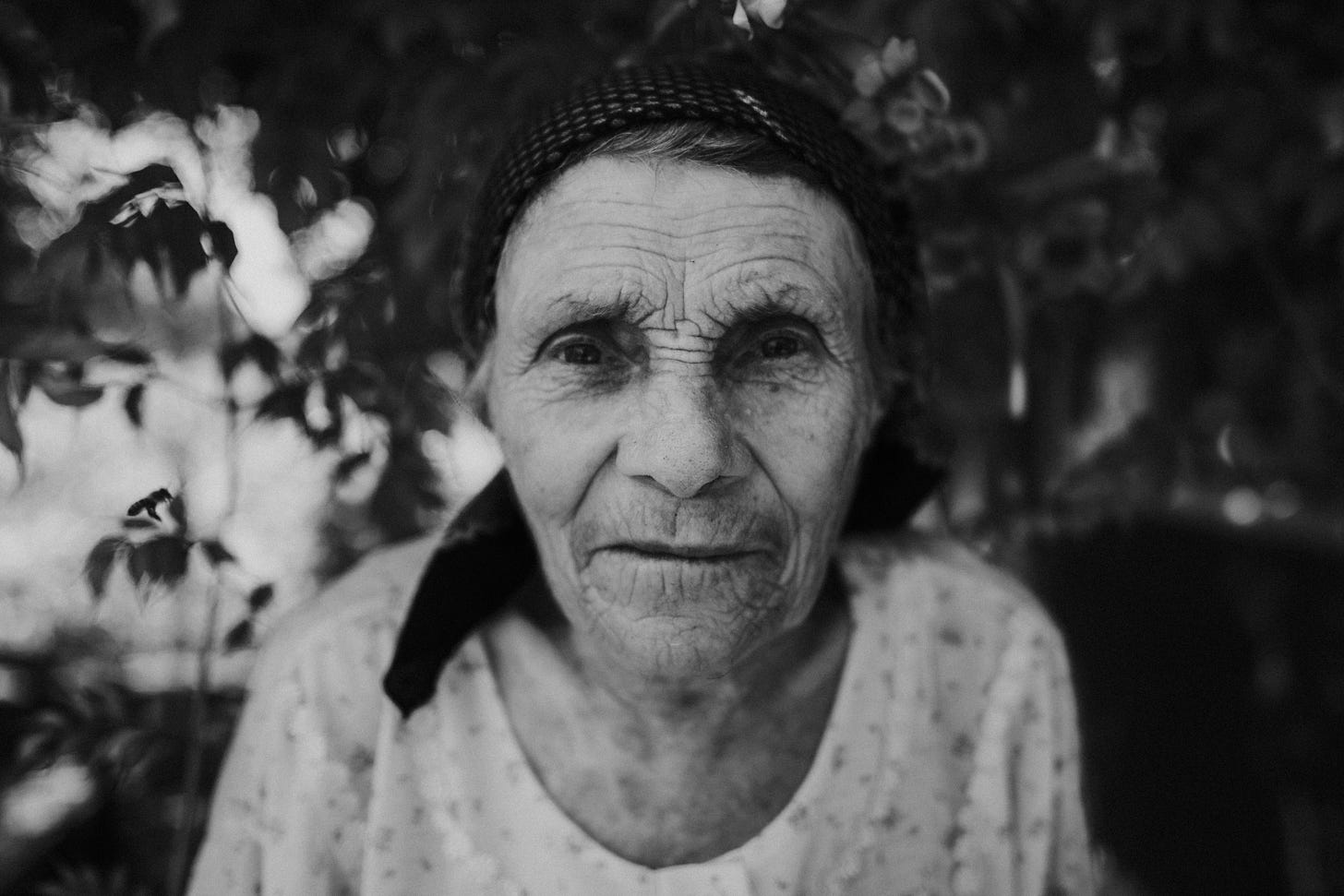 Photograph of an elderly woman, staring directly at the camera, with an inscrutable yet kindly expression.