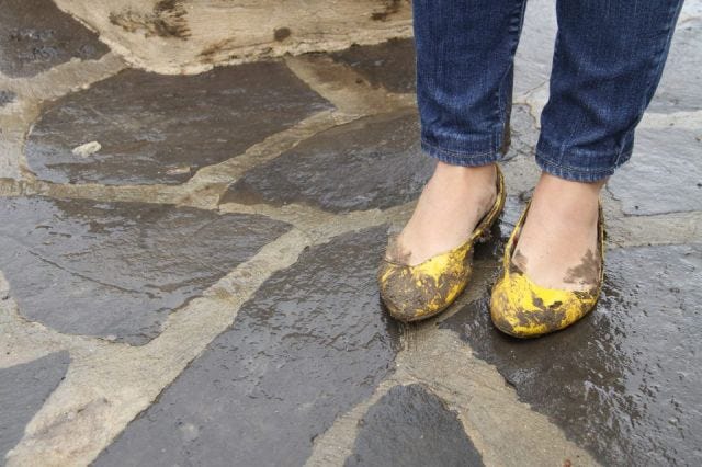 Snapshot of muddy, yellow shoes on wet concrete.