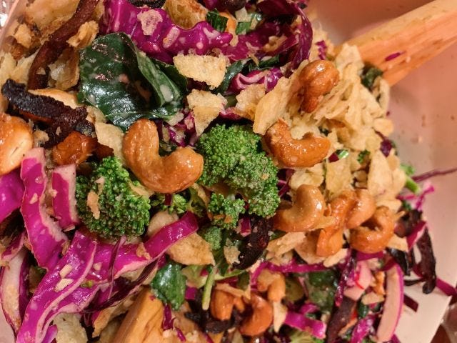 A mess of broccoli, red cabbage, cashews, and chips in a bowl