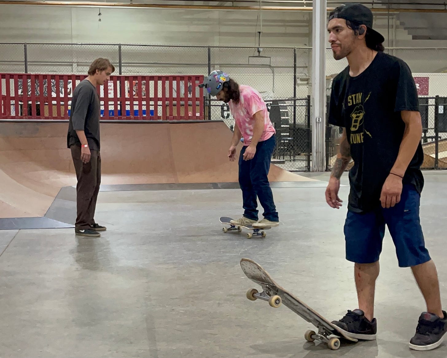 Bennett Sizer (left) teaching Blind Skater, Anthony Ferraro (middle) how to do a flip trick as Blind Skater, Jon Baron (right) kicks up his skateboard to walk by