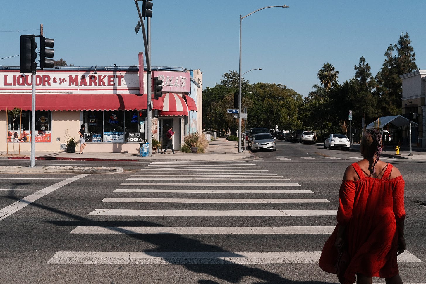 Woman in red dress walks across the street, in a cross walk, in Los Angeles California.