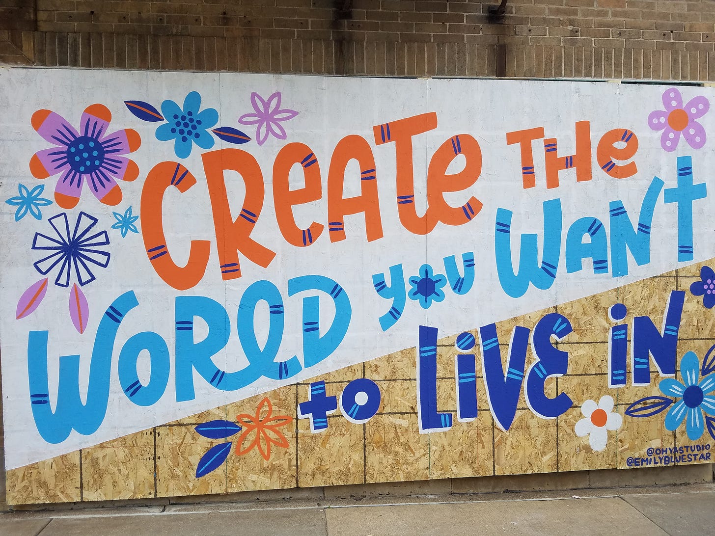 A brightly colored mural painted on plywood reads "Crate the world you want to live in."