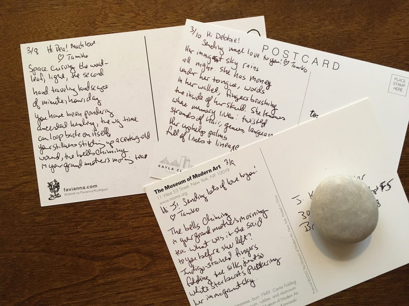 Three postcards with poems written on the back. A smooth, round stone holds them down.