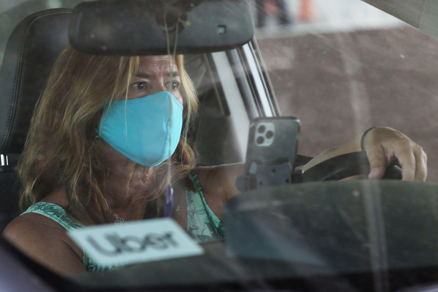 A white woman wearing a light blue cloth mask drives an Uber 