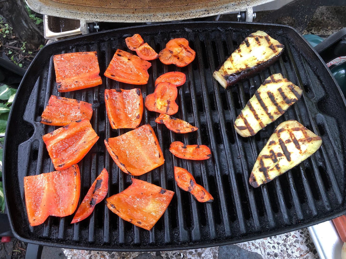 Slices of red pepper and eggplant on a small propane grill. Both vegetables have moderate charring and look throughly cooked. 