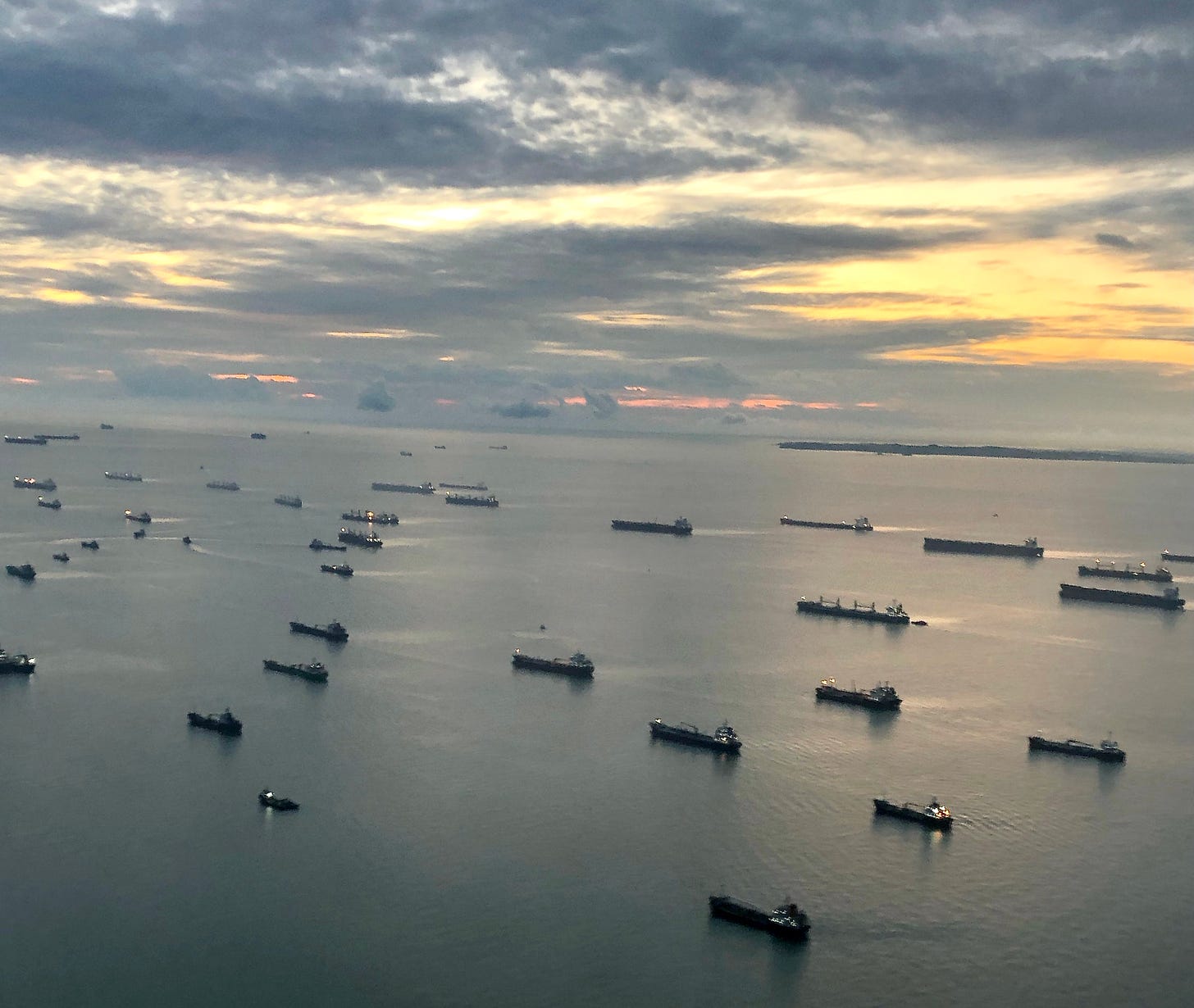 dozens of shipping vessels in the Singapore Strait seen from the air at sunrise