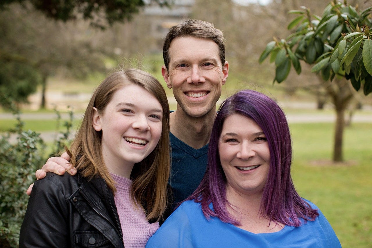 Stella Keating, 16 year old female trans student, posing for a picture with her mother and father, all smiling towards the camera and looking very happy