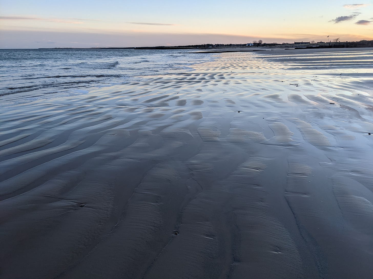 Wavy lines in the wet sand at low tide with the sunrising in the distance