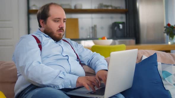 Funny Fat Man Working on Laptop Sitting on Couch at Home by nimito