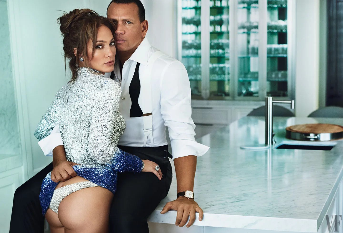 Alex Rodriguez is sitting on the edge of a big marble kitchen island, with Jennifer Lopez standing in between his legs. They're both looking at the camera, and he is pulling her dress up to reveal her underwear. 