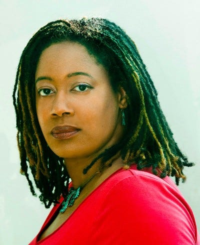 Angled portrait of N.K. Jemisin with a neutral expression on her face, looking to the camera, wearing a read shirt.