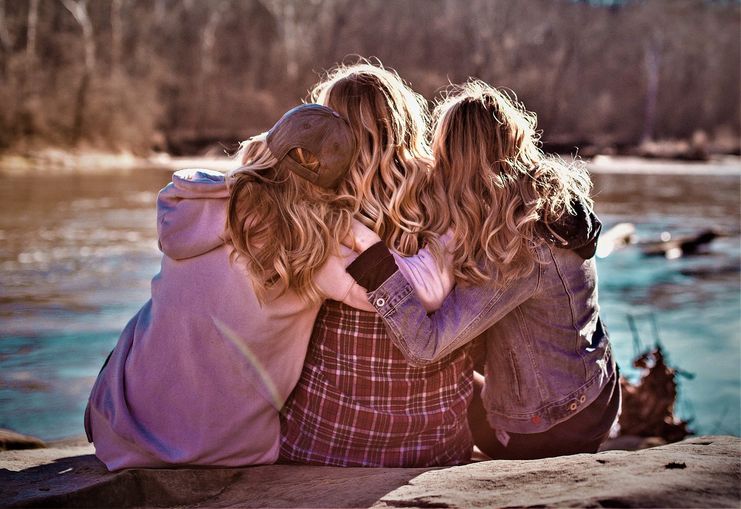 rear view of three girls with long blonde hair with arms around each other looking out at lake