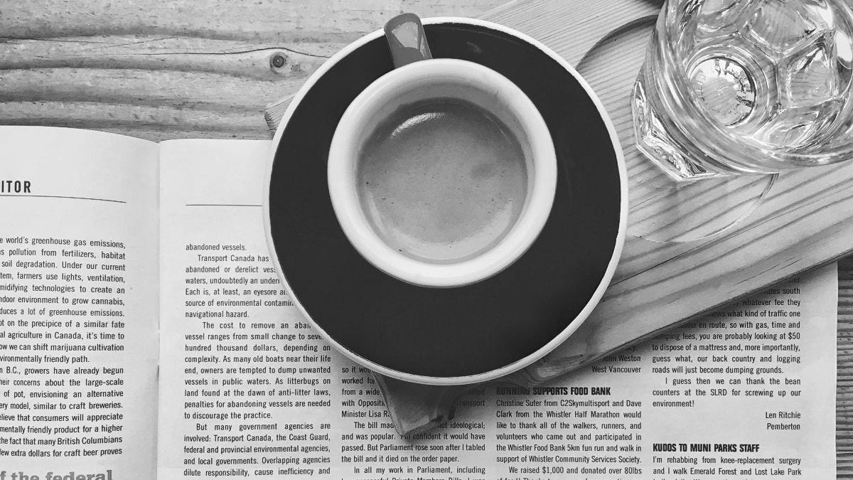 An espresso cup containing coffee sits atop a magazine on a table, seen from above.