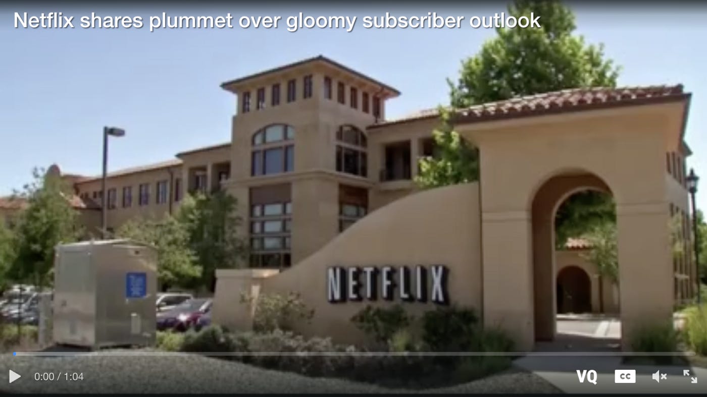 Image description: A picture of large building that is painted a sandy color with a terracotta tile roof. A Netflix sign is on the front wall. Above is a blue sky. Text at the top of the image reads: “Netflix shares plummet over gloomy subscriber outlook”