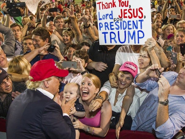 A huge crowd of smiling white people greets then-candidate Donald Trump. A sign in the crowd reads "Thank You Lord Jesus For President Trump."