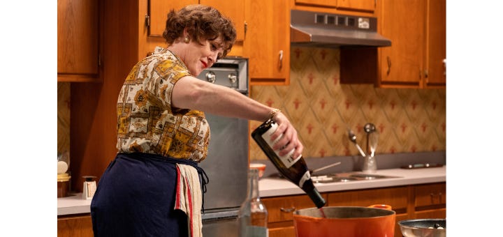 Actress playing Julia Child pouring wine into a pot in a kitchen