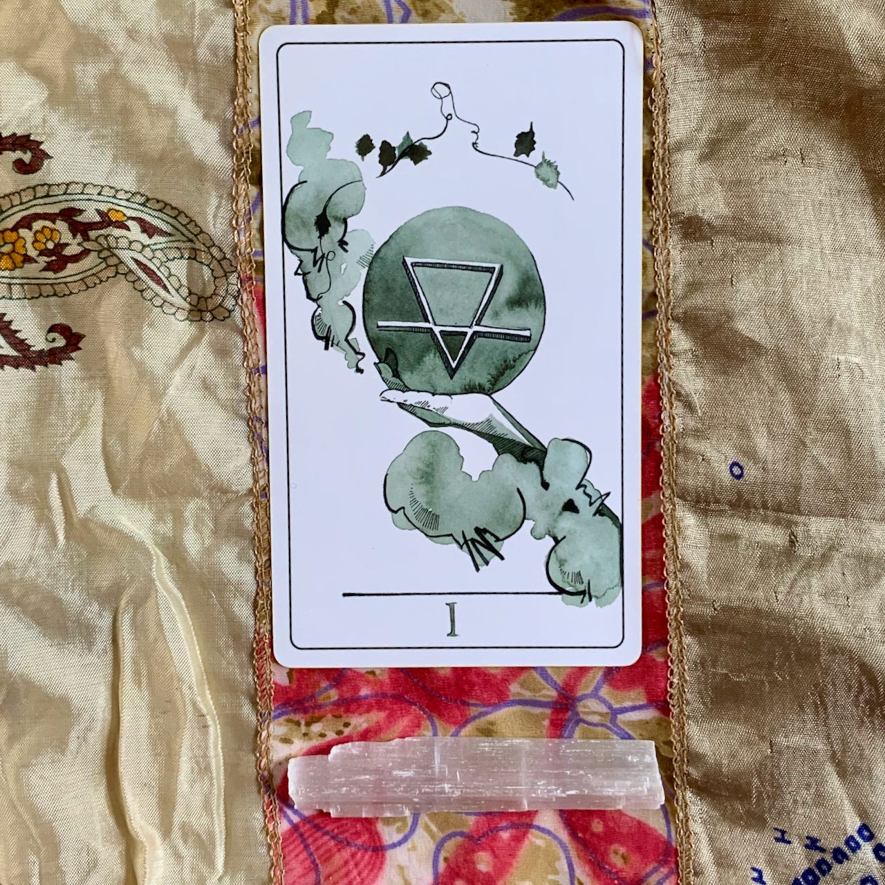ace of cups tarot card on a cream and red background above a selenite crystal