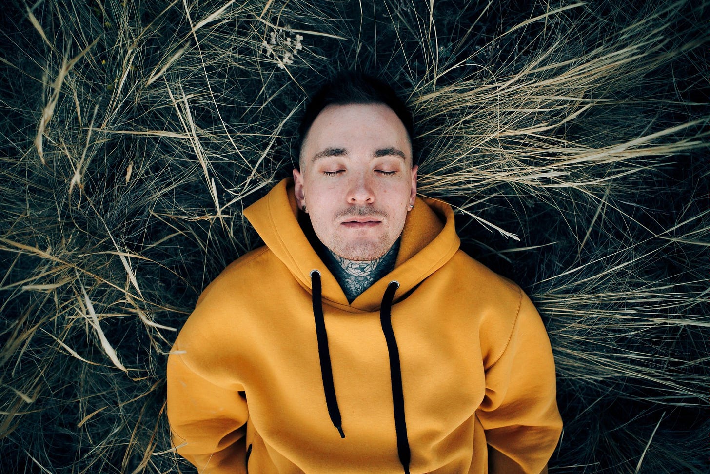 A man in a yellow hoodie lays in long grass.