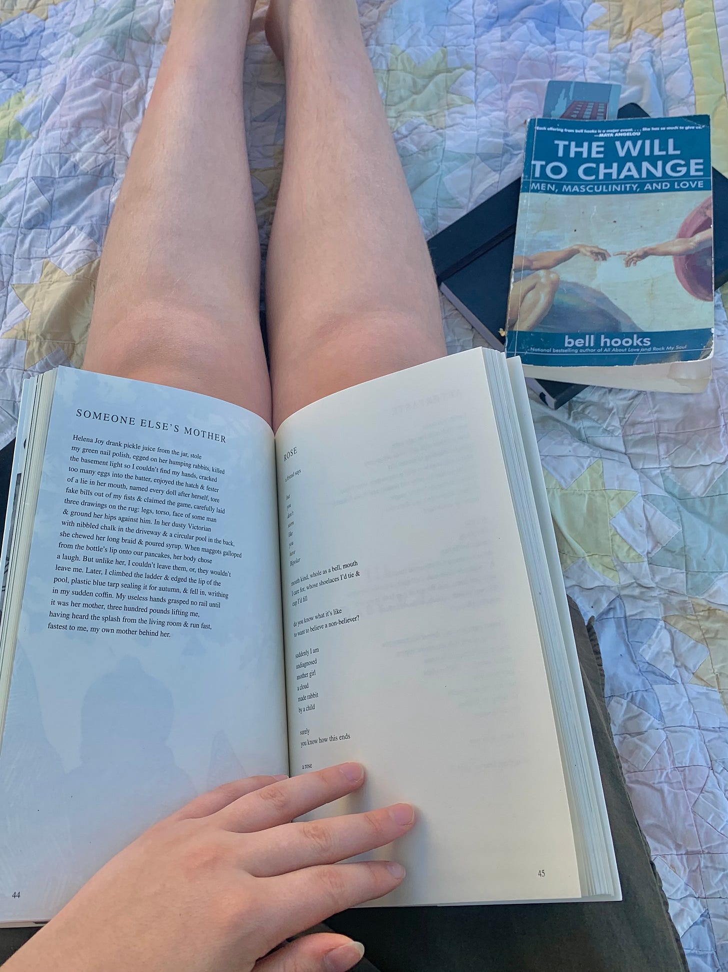 a photo of mira's legs with a book open on their lap. beside them a copy of "the will to change" by bell hooks rests on top of a black journal.