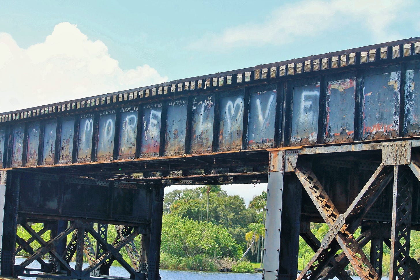 Old steel railroad bridge that says more love in white paint