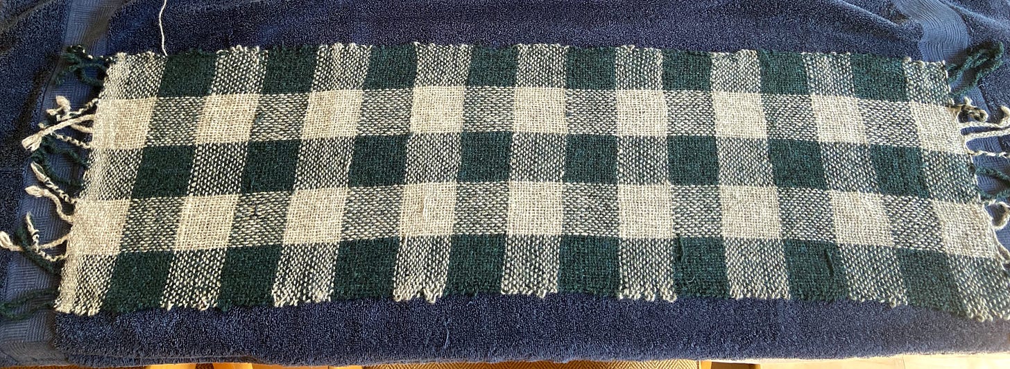 a green and gray plaid scarf with a large weave, drying on a towel.