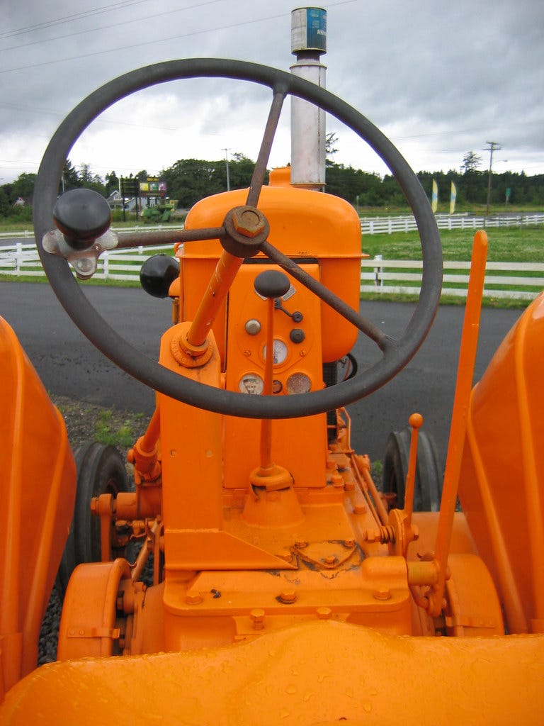 View from driver's seat of an orange tractor. "Orange Tractor" by spaceninja is licensed under CC BY-NC-SA 2.0 