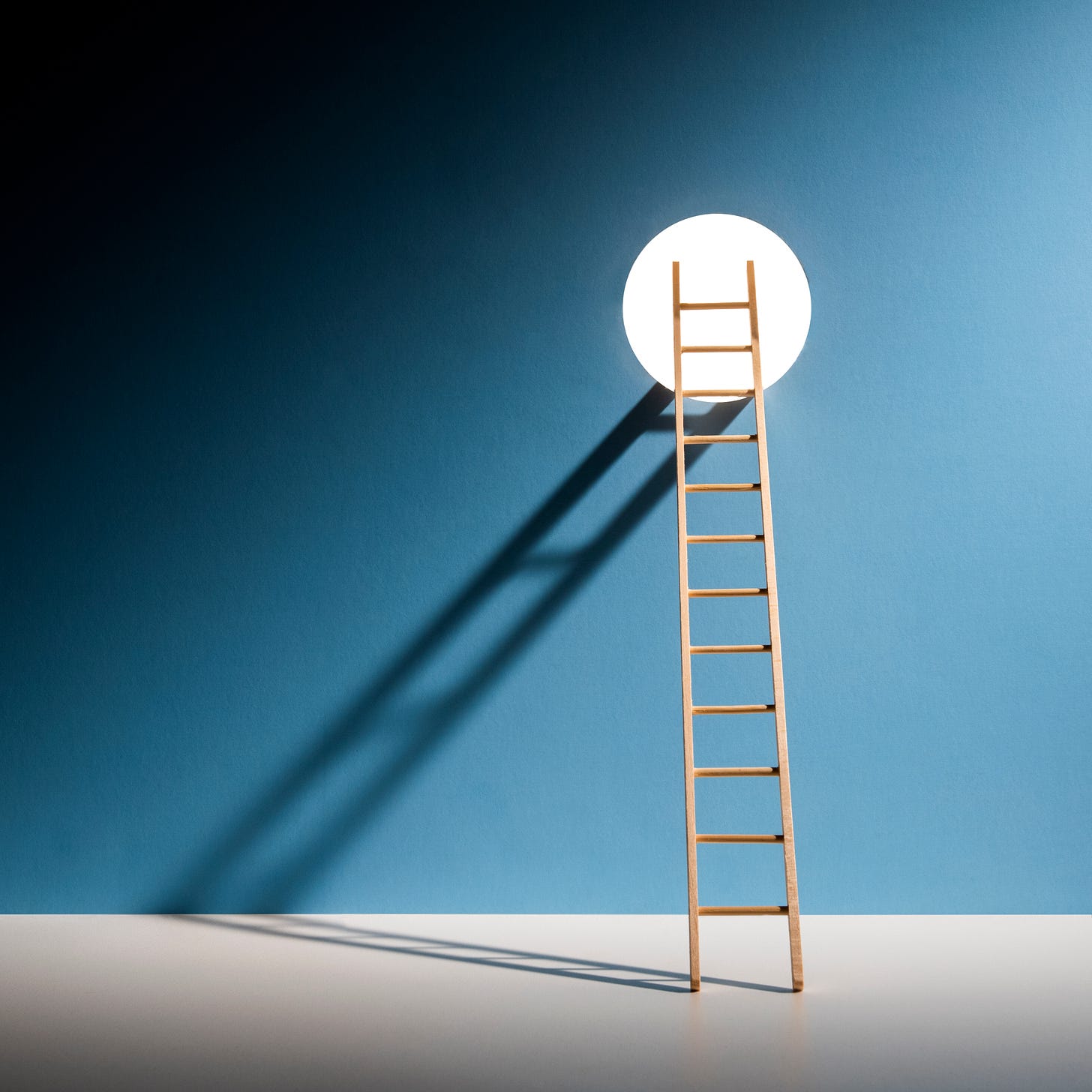 Ladder propped against a white circle on a blue wall with the shadow of the ladder cascading to the left