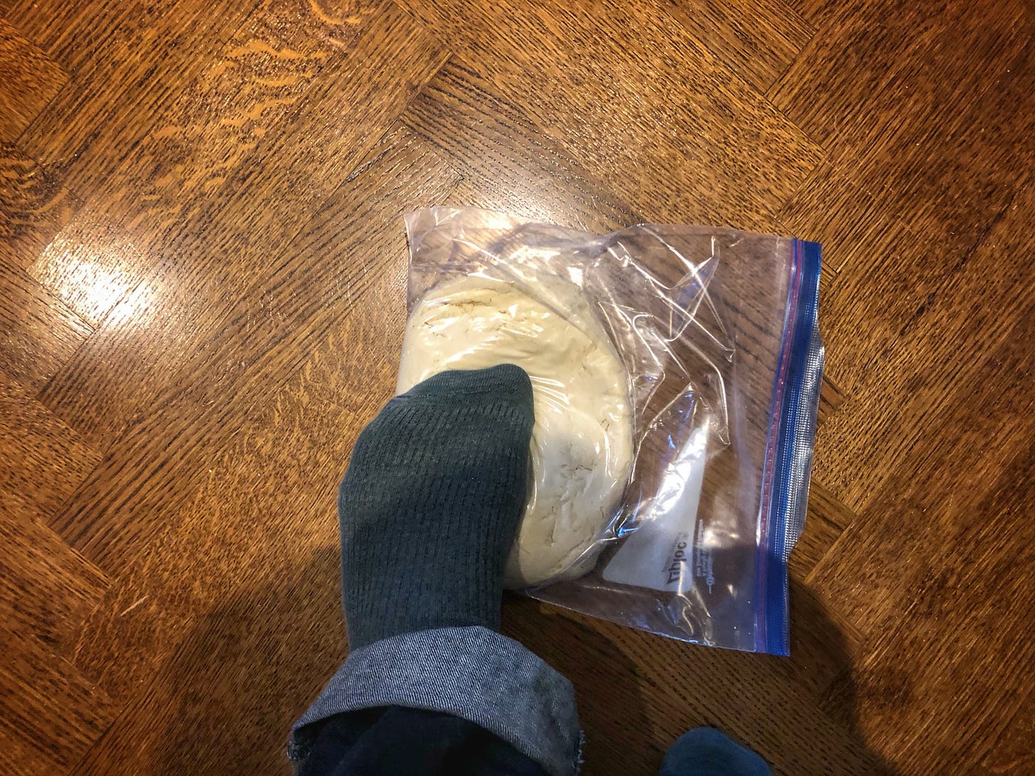 A foot stepping on a dough ball in a Ziploc bag
