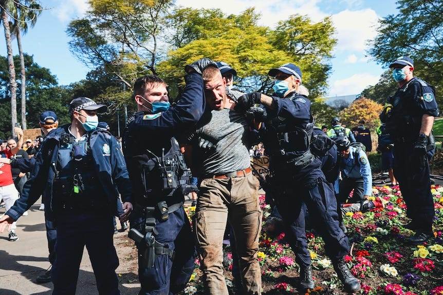 Several police officers grabbing a man, who is shouting.