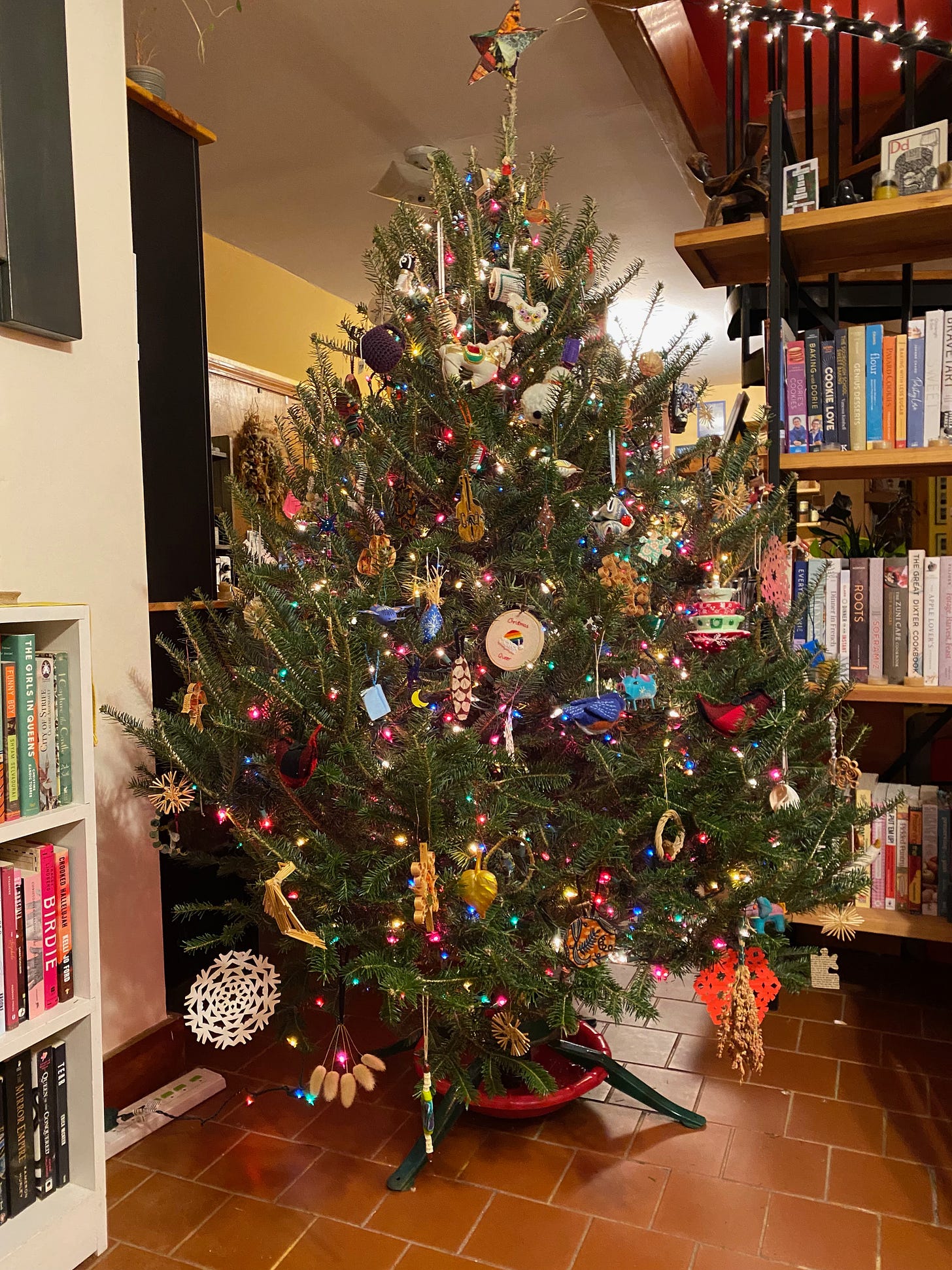 A Christmas tree full of colored lights and ornaments stands between two bookshelves.