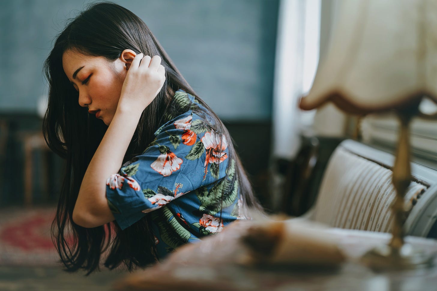 A pretty young woman stares pensively at the ground as she tucks her hair behind her ears.