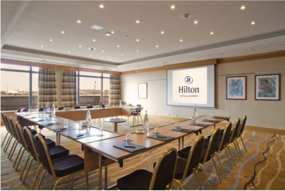 A hotel meeting room showing some meeting tables and chairs and a projection screen.