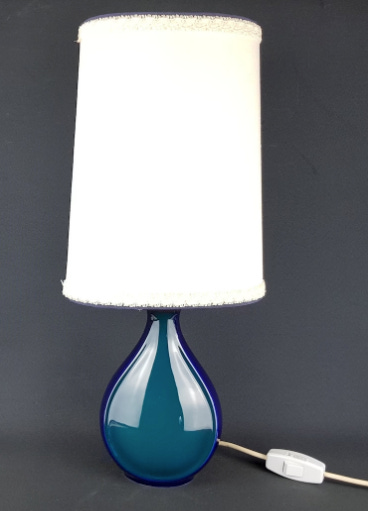 A glossy ceramic vase, glazed blue, with a tall white lampshade