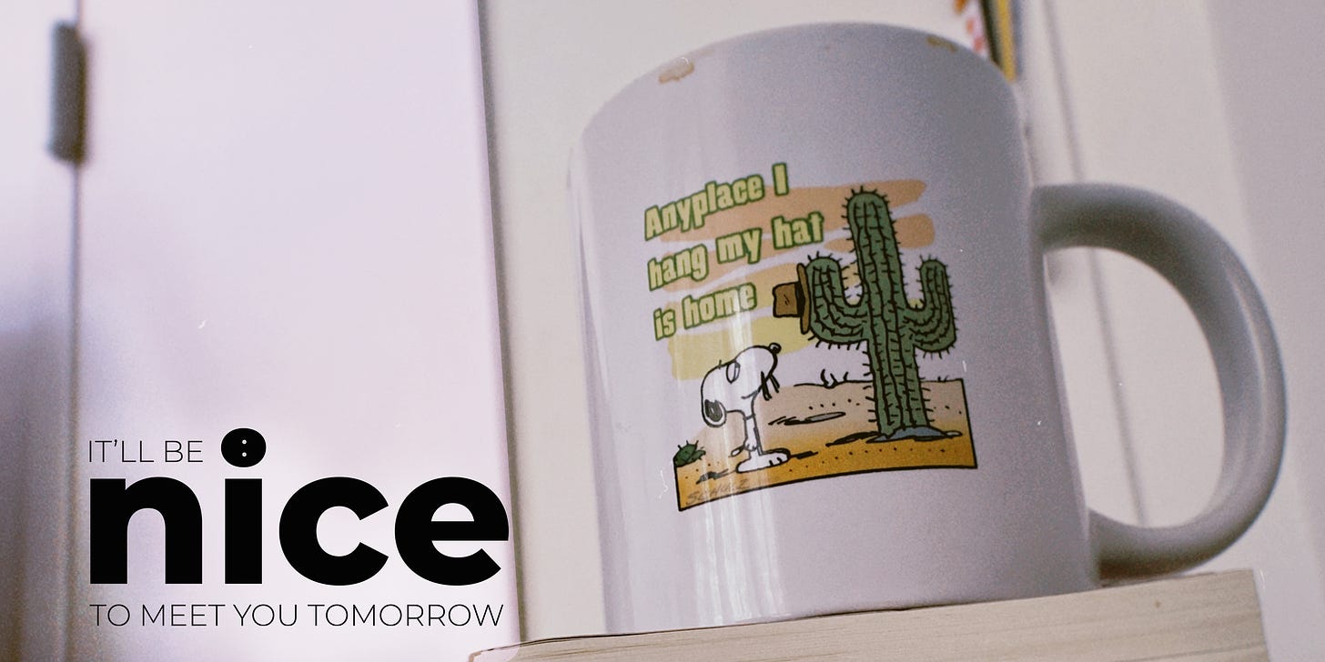 A white ceramic mug that says "Anyplace I hang my hat is home." with Snoopy's brother Spike drawn on it. He has hung his hat on a cactus in the desert. The image also has the logo for It'll Be Nice To Meet You Tomorrow in the lower left corner.