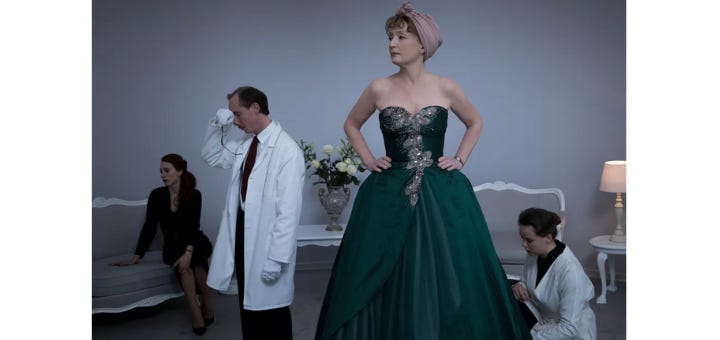 a woman in a strapless green ball gown with her hands on her hips, at a dress fitting