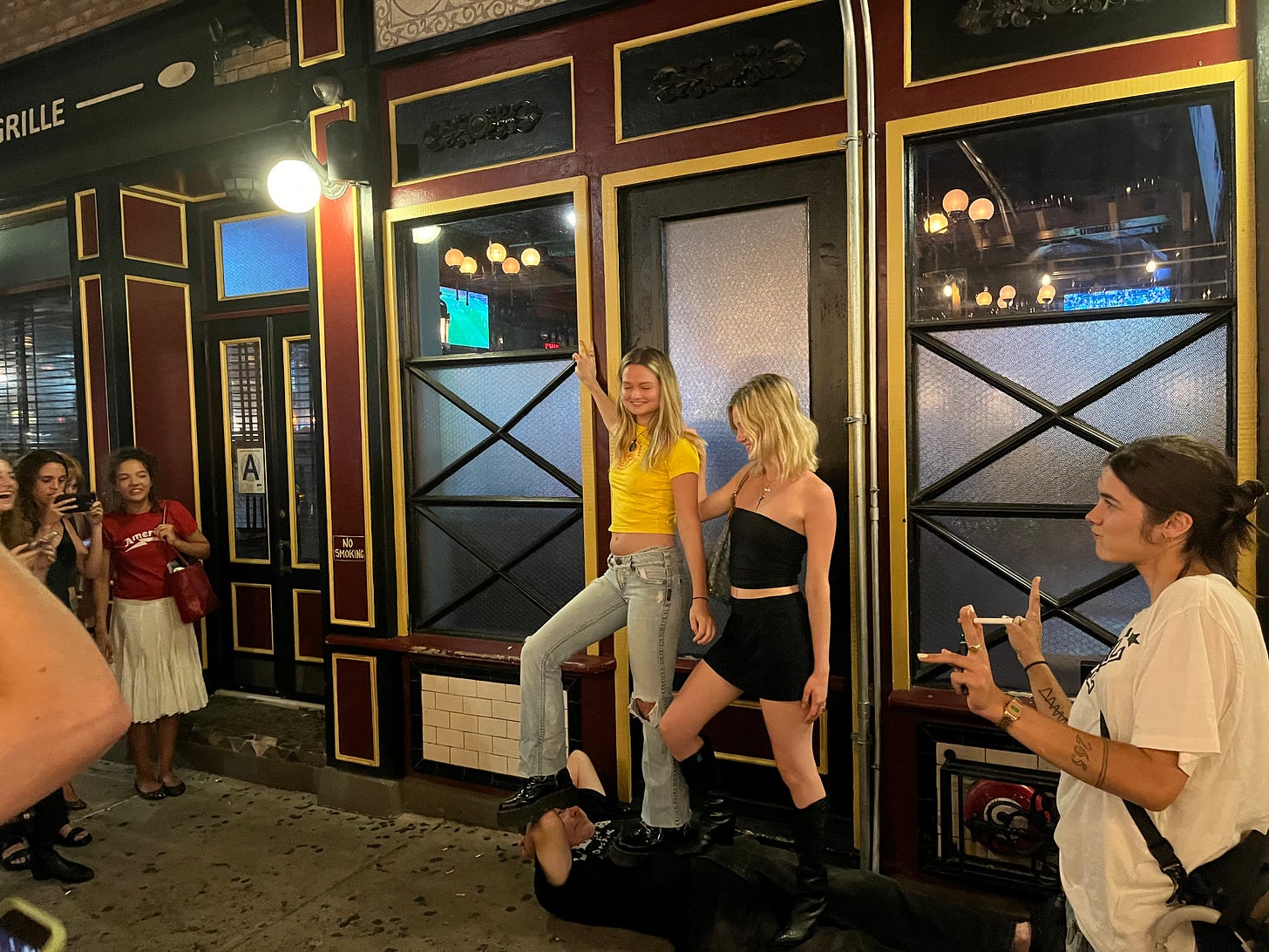Two girls stand on top of a man outside a bar in the Lower East Side