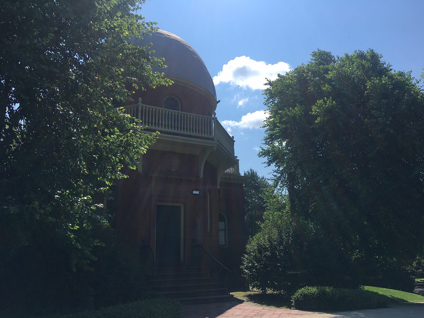 A domed brick building surrounded by trees on a sunny day