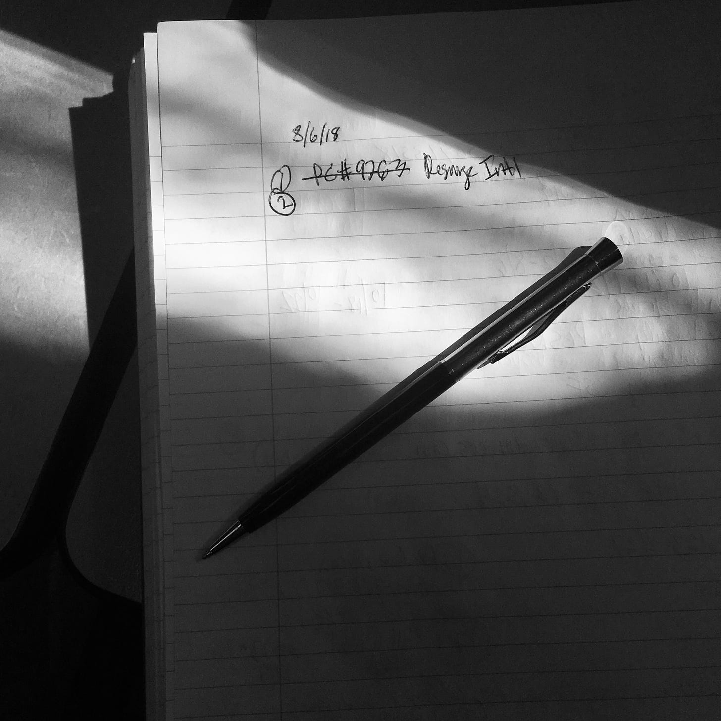 Close-up photo of a pen and notebook with a ray of light across the  frame. The notebook has a handwritten notes with the date 3/16/18  and scribbles of numbers and letters.