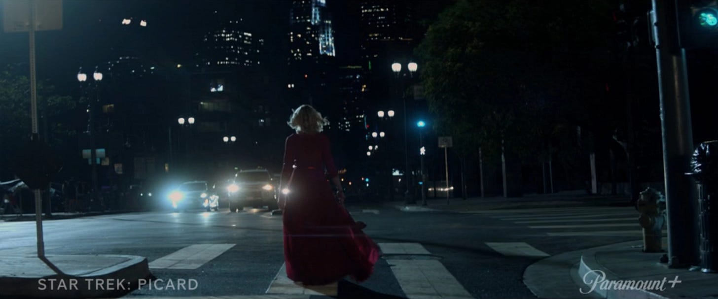 This image shows Agnes Jurati (played by Alison Pill) strolling down a city street at night in 2024 Los Angeles. Jurati's back is to camera as her red party dress trails behind her. This image shows Agnes Jurati (played by Alison Pill) strolling down a city street at night in 2024 Los Angeles. Jurati's back is to camera as her red party dress trails behind her.