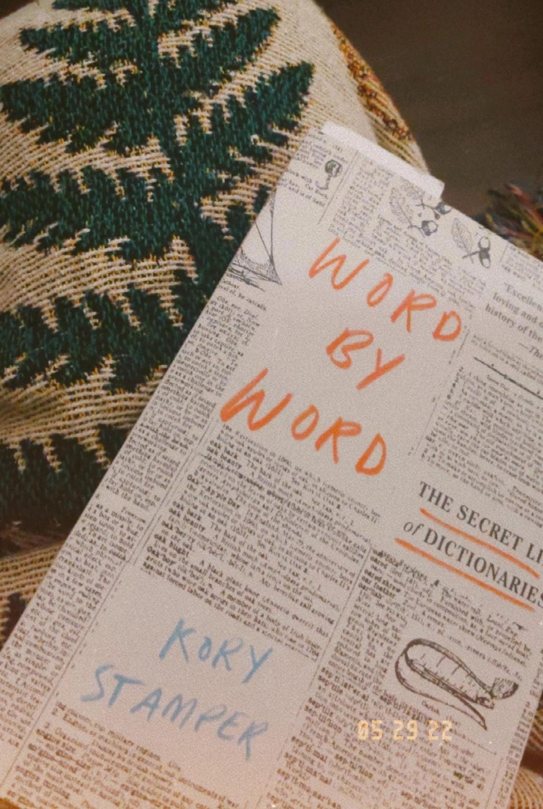 The book Word by Word, on a blanket embroidered in the shape of a fern leaf