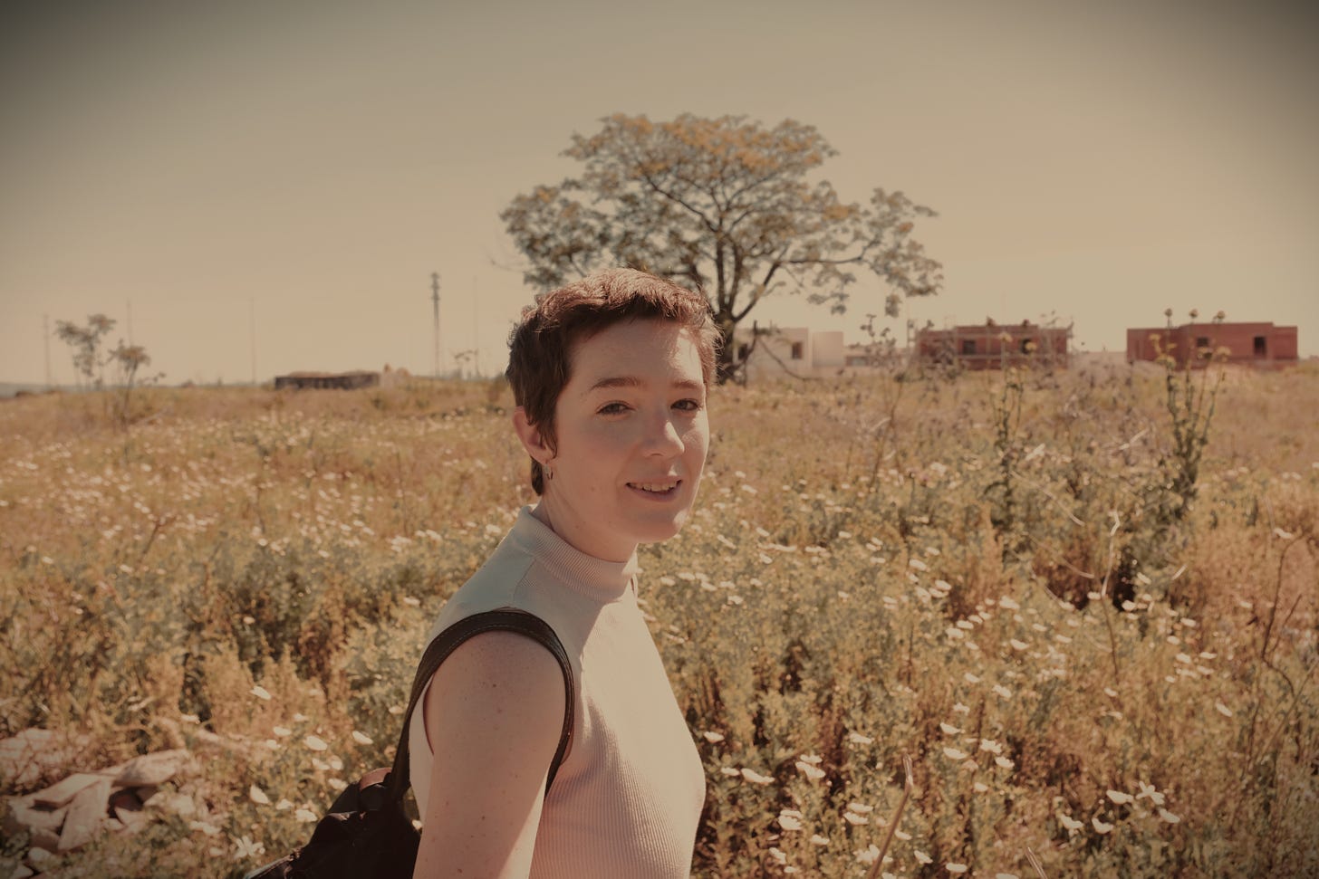 A picture of me, a goofy slim white lady with short hair and crooked teeth. A rose tinted view of an Andalusian spring scene that looks like summer somewhere else.
